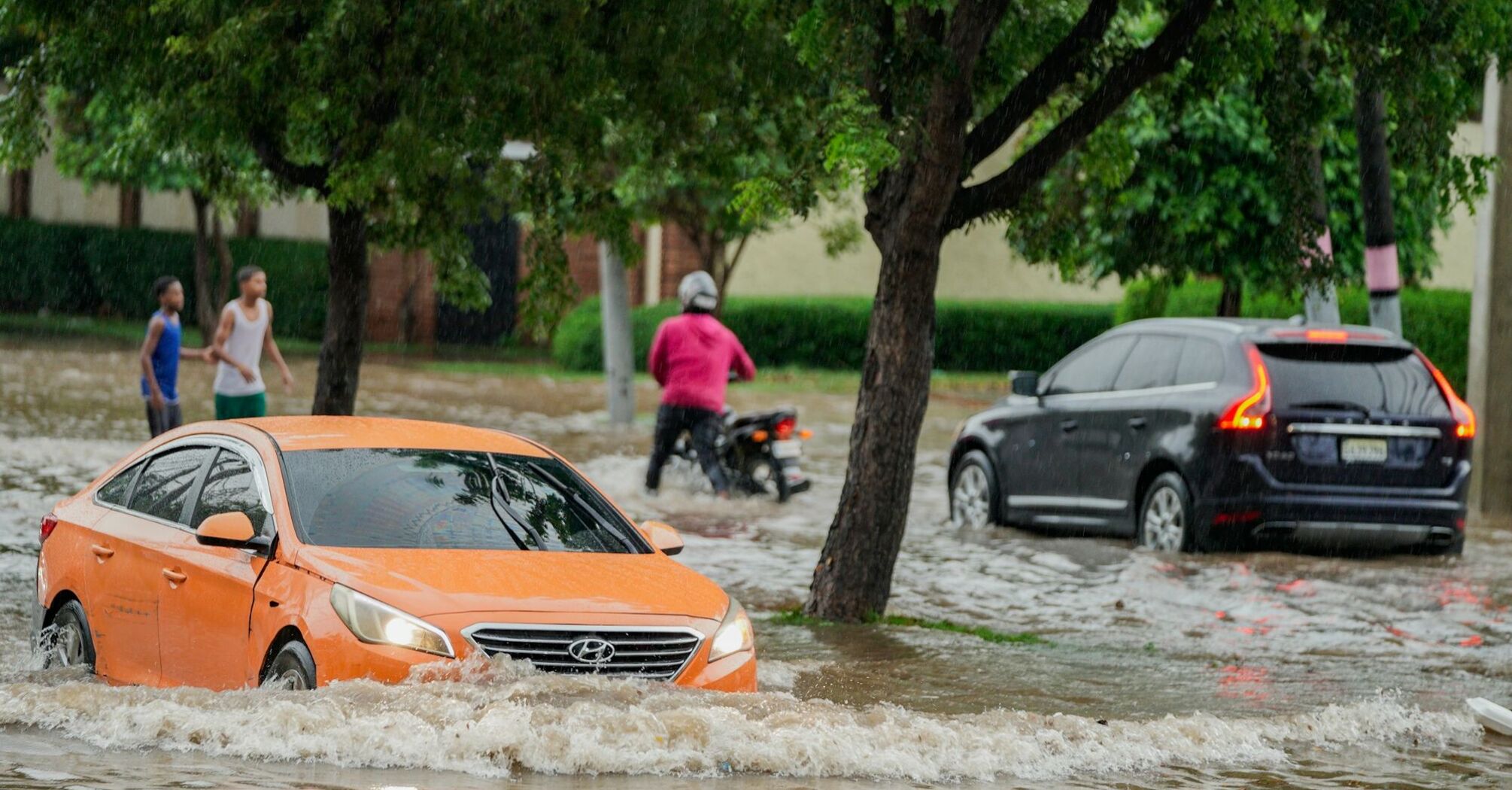 Cars and pedestrians navigating flooded streets after heavy rain