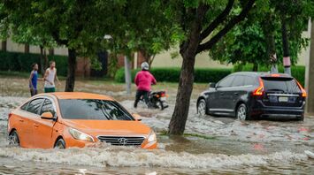 Cars and pedestrians navigating flooded streets after heavy rain