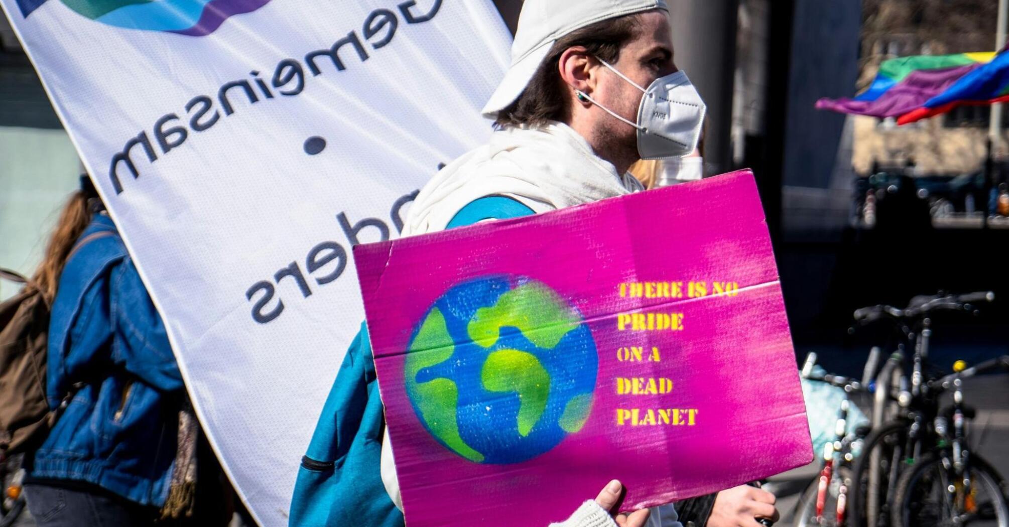 A participant holds a sign with a planet illustration and a message about environmental responsibility