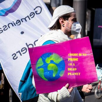 A participant holds a sign with a planet illustration and a message about environmental responsibility