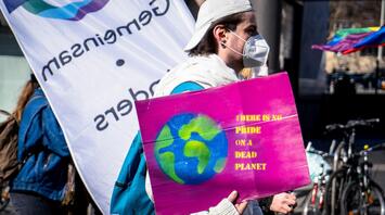 A participant holds a sign with a planet illustration and a message about environmental responsibility