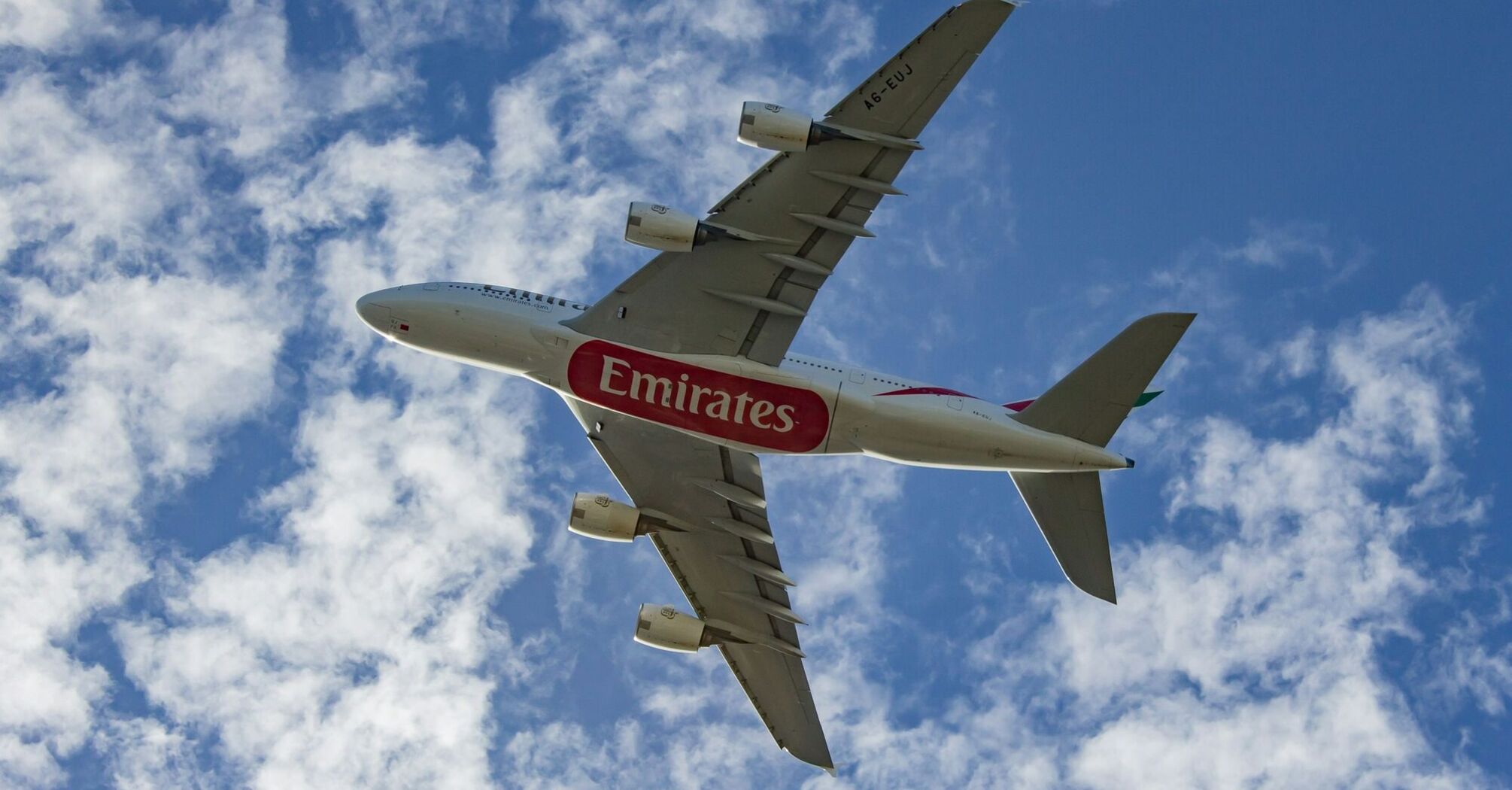 Emirates aircraft flying against a blue sky with clouds