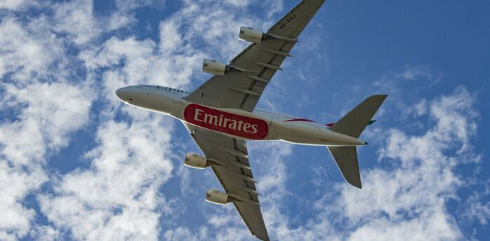 Emirates aircraft flying against a blue sky with clouds