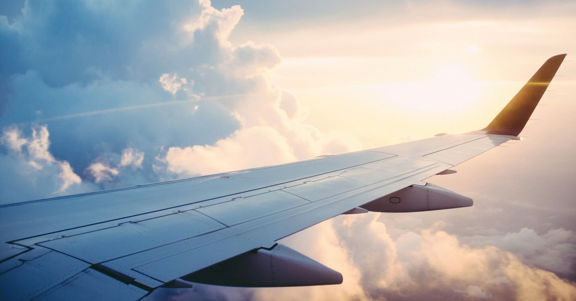 A view from an airplane window showing the wing against a backdrop of clouds and sunlight