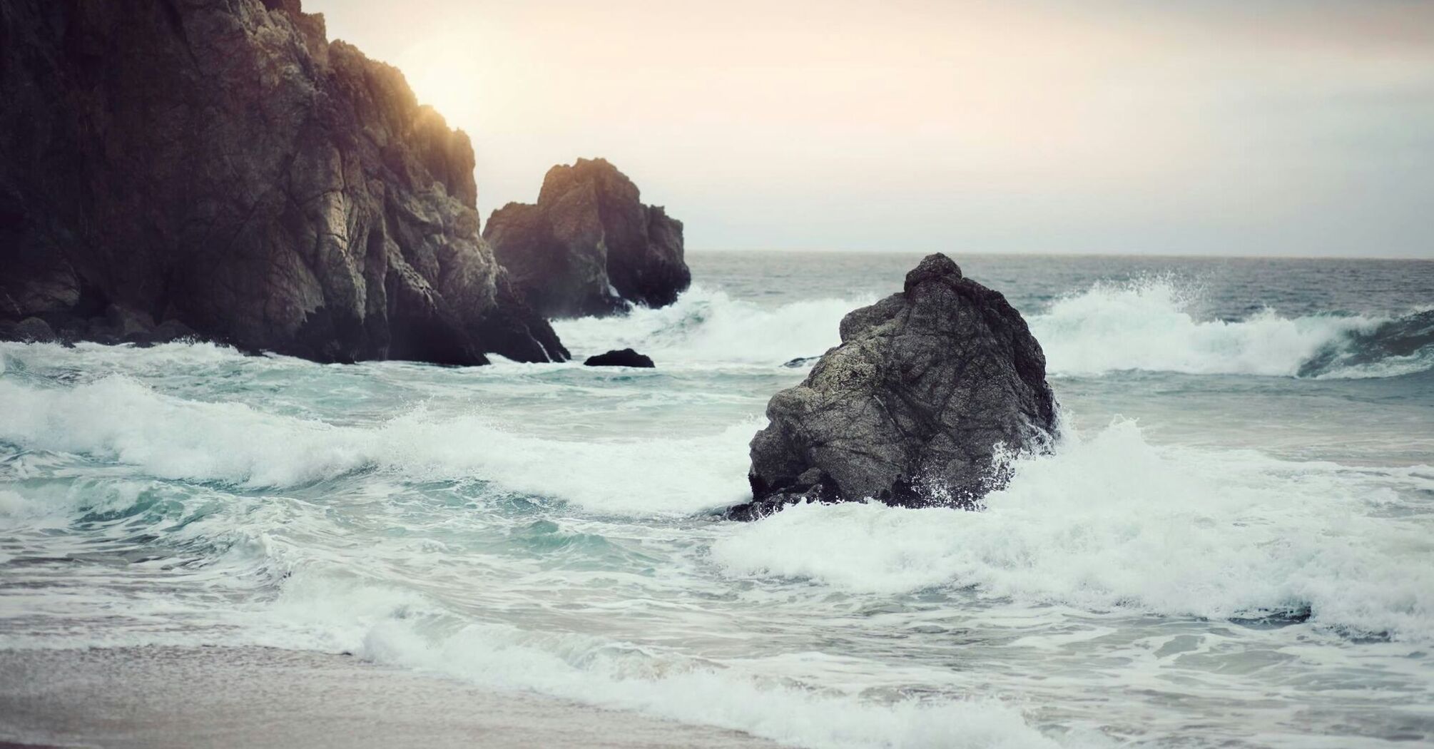 Waves crashing against rocky shore at sunset