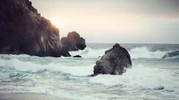 Waves crashing against rocky shore at sunset