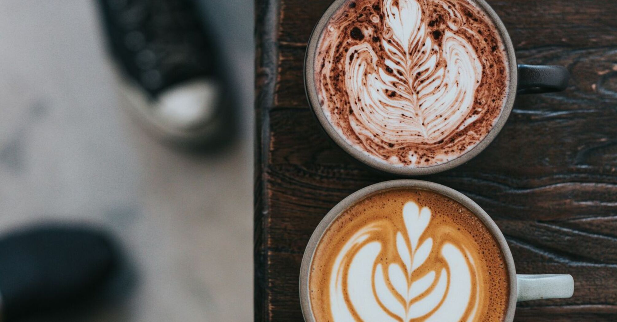 Two cups of coffee with intricate latte art placed on a wooden table