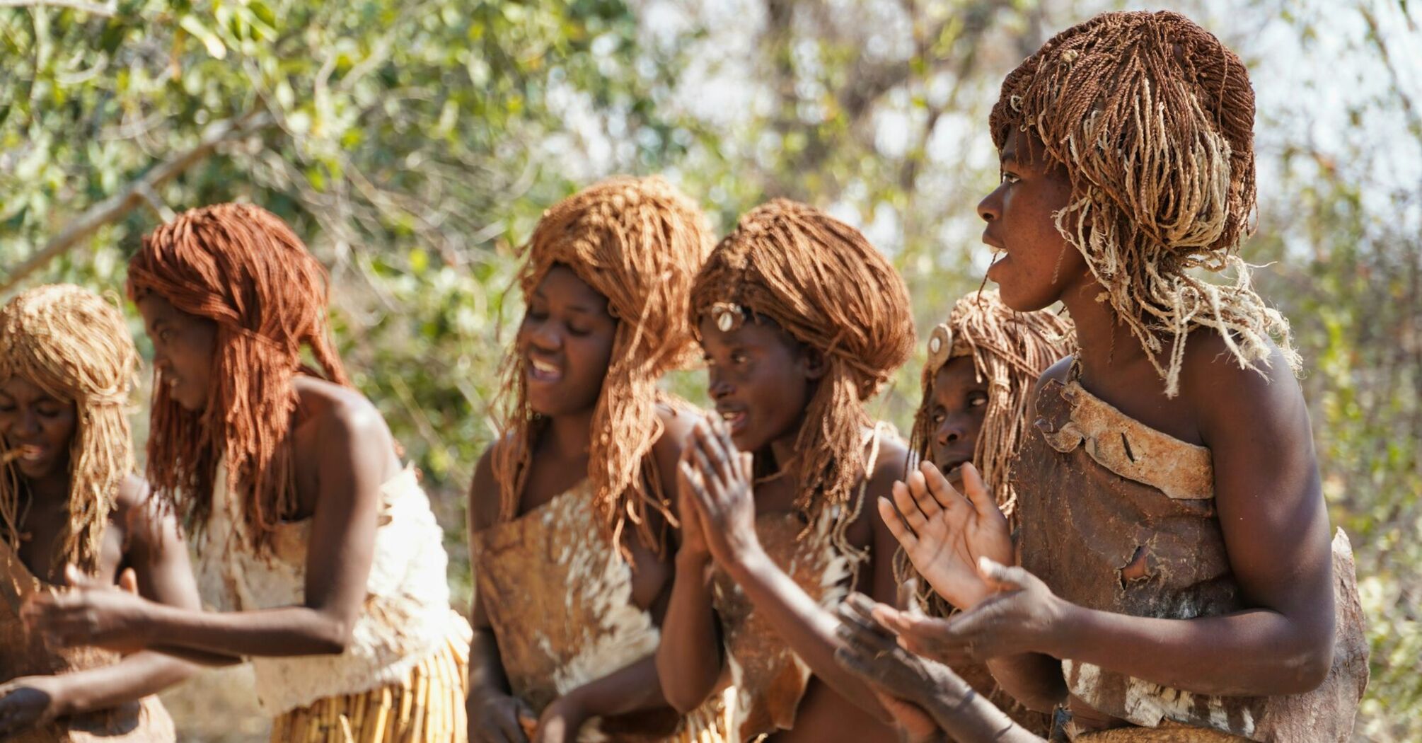 A group of African women in Namibia region in traditional attire, clapping and singing in a natural outdoor setting