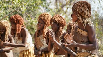 A group of African women in Namibia region in traditional attire, clapping and singing in a natural outdoor setting