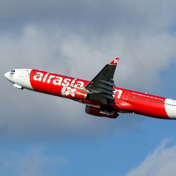A red and white AirAsia airplane taking off against a backdrop of cloudy skies