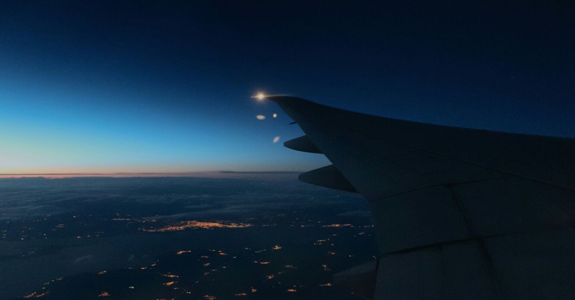 Nighttime view of an airplane wing over a lit-up city below