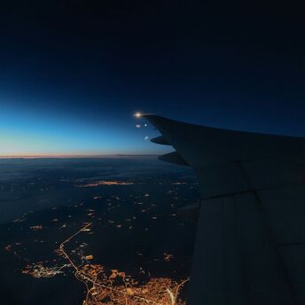 Nighttime view of an airplane wing over a lit-up city below