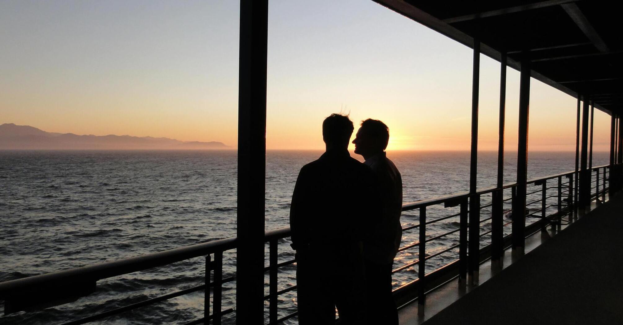 Two passengers looking at the sunset from a cruise ship deck