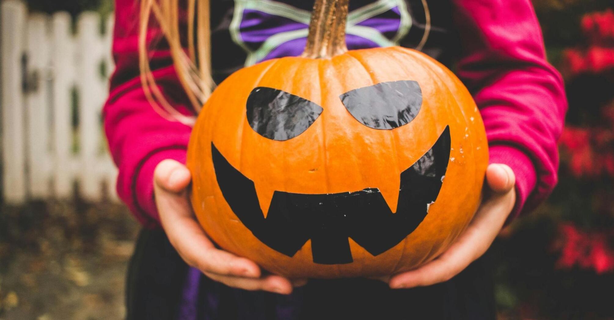 Child holding a carved pumpkin with a spooky face