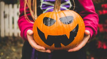 Child holding a carved pumpkin with a spooky face