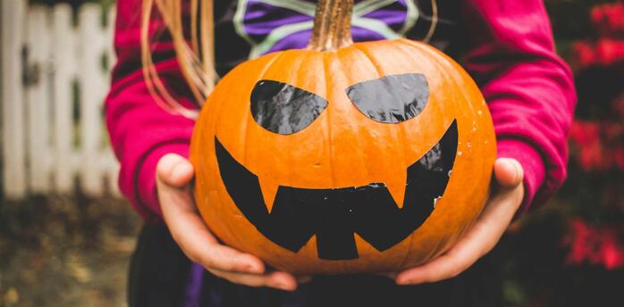Child holding a carved pumpkin with a spooky face