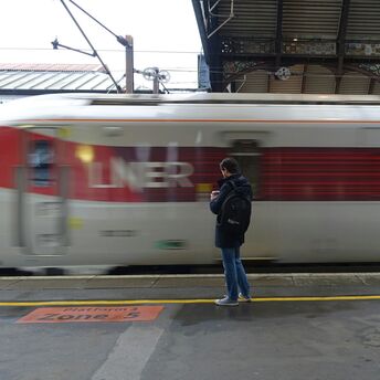 A man stands on a train platform as an LNER train speeds past, creating a blurred motion effect