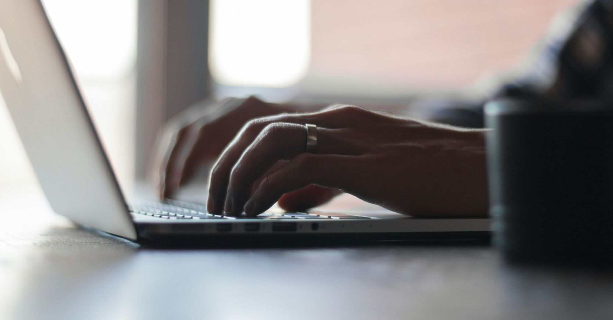 Hands typing on a laptop keyboard in a dimly lit room