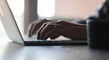 Hands typing on a laptop keyboard in a dimly lit room