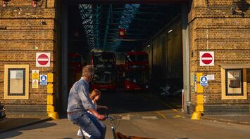 A cyclist with a child passes by a Stagecoach depot with several red buses parked inside