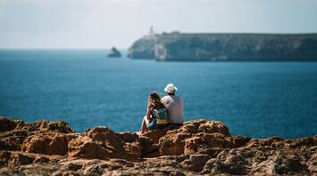 A couple sitting on rocky cliffs overlooking the ocean at Sagres, Portugal
