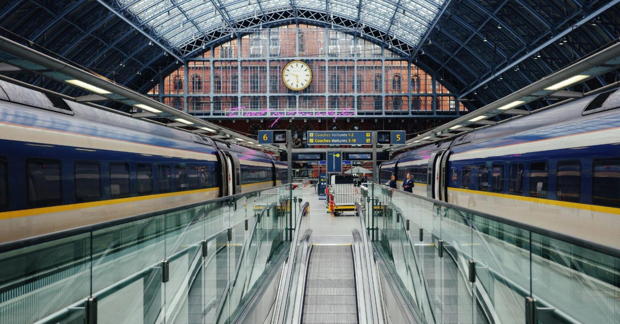 Eurostar trains stationed under the glass roof of a European terminal, with walkways leading to boarding platforms