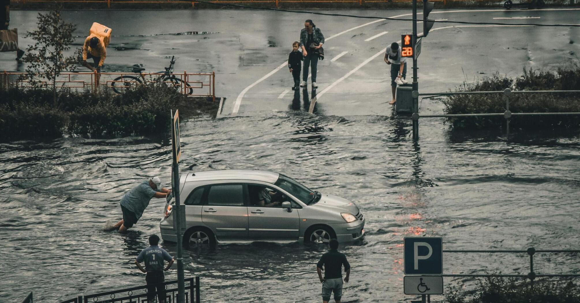 People wading through flooded streets and pushing a car during heavy rain