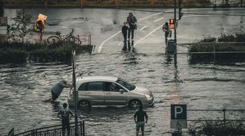People wading through flooded streets and pushing a car during heavy rain