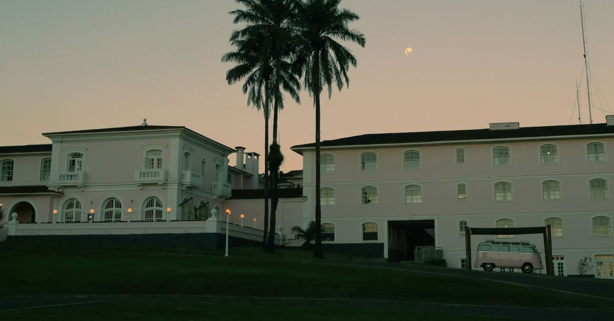 A classic building with palm trees at dusk, with a pale moon visible in the sky