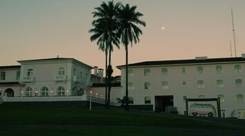 A classic building with palm trees at dusk, with a pale moon visible in the sky