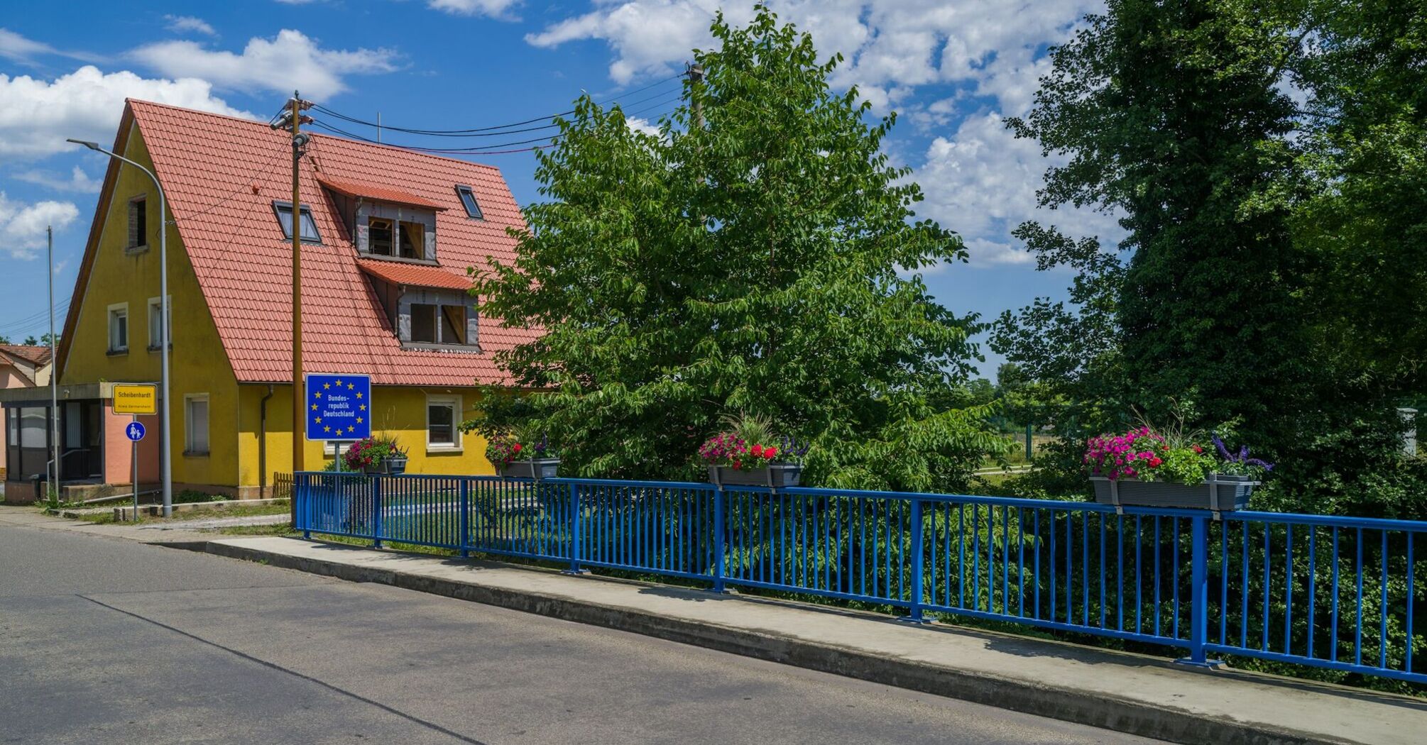 A peaceful town at the French-German border with a yellow house, blue railing, and a European border sign