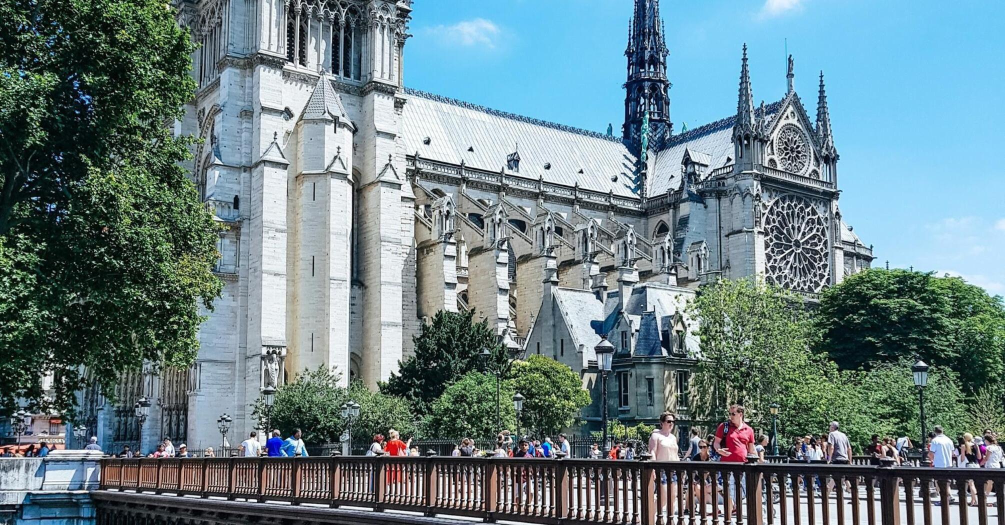 Notre Dame Cathedral viewed from across a bridge filled with pedestrians on a sunny day