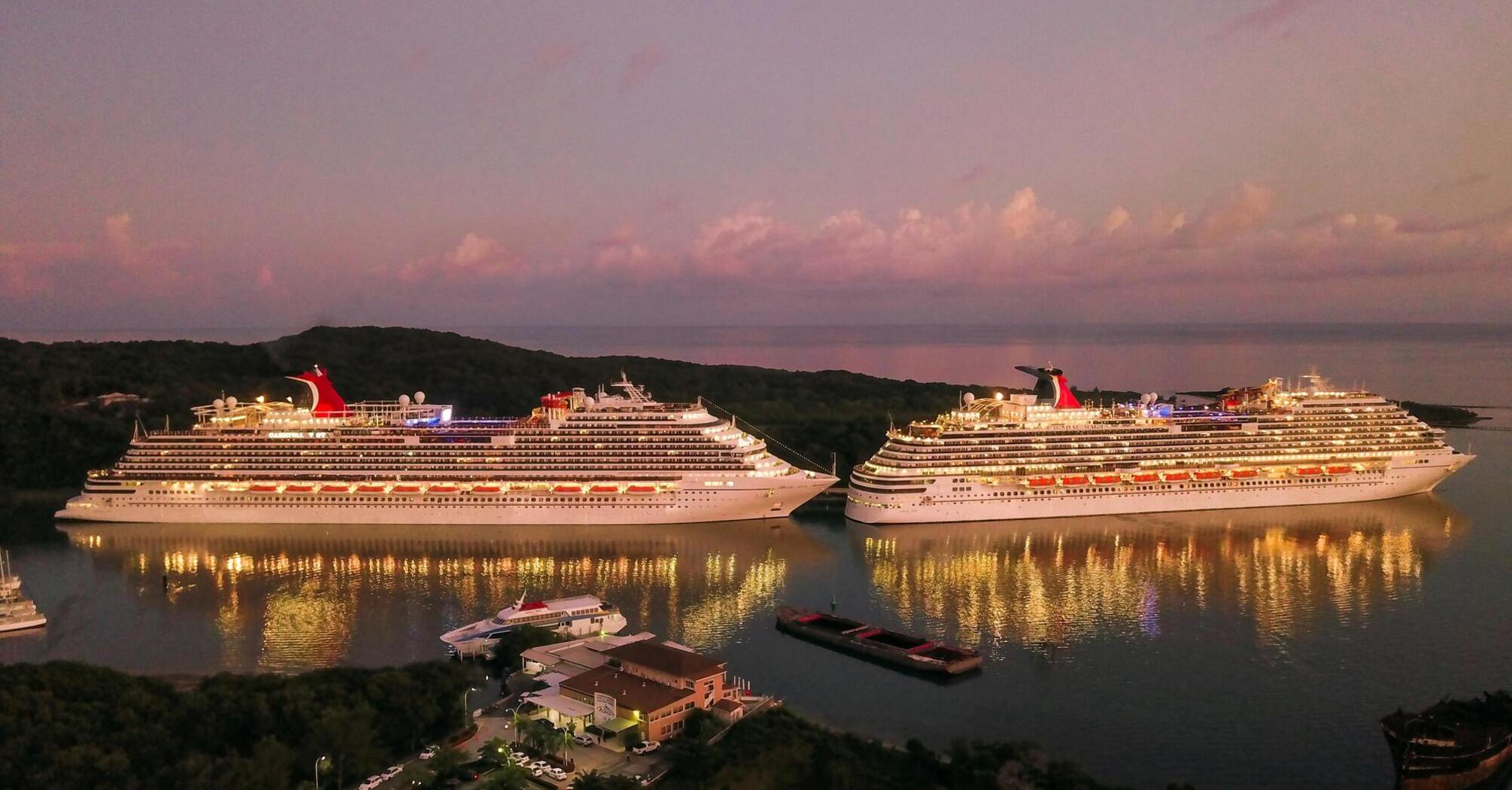 Two illuminated cruise ships docked at sunset