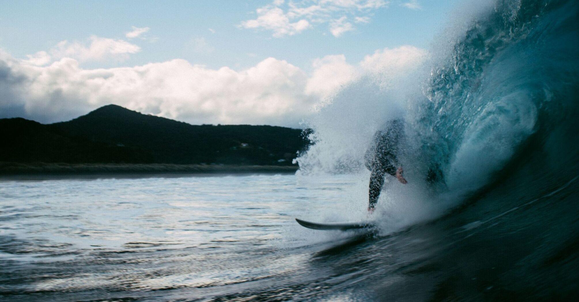 Surfer riding a wave near a mountainous coast