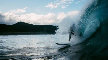Surfer riding a wave near a mountainous coast