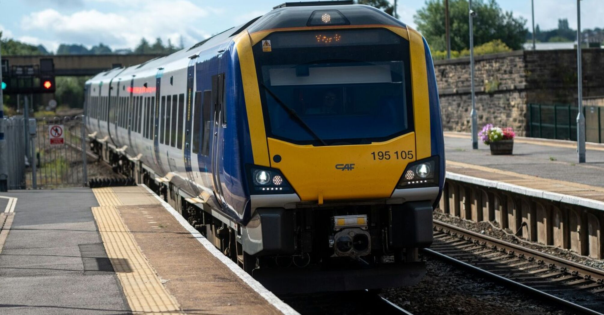 A blue and yellow passenger train at Leeds station platform under a cloudy sky