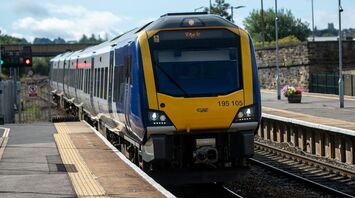 A blue and yellow passenger train at Leeds station platform under a cloudy sky