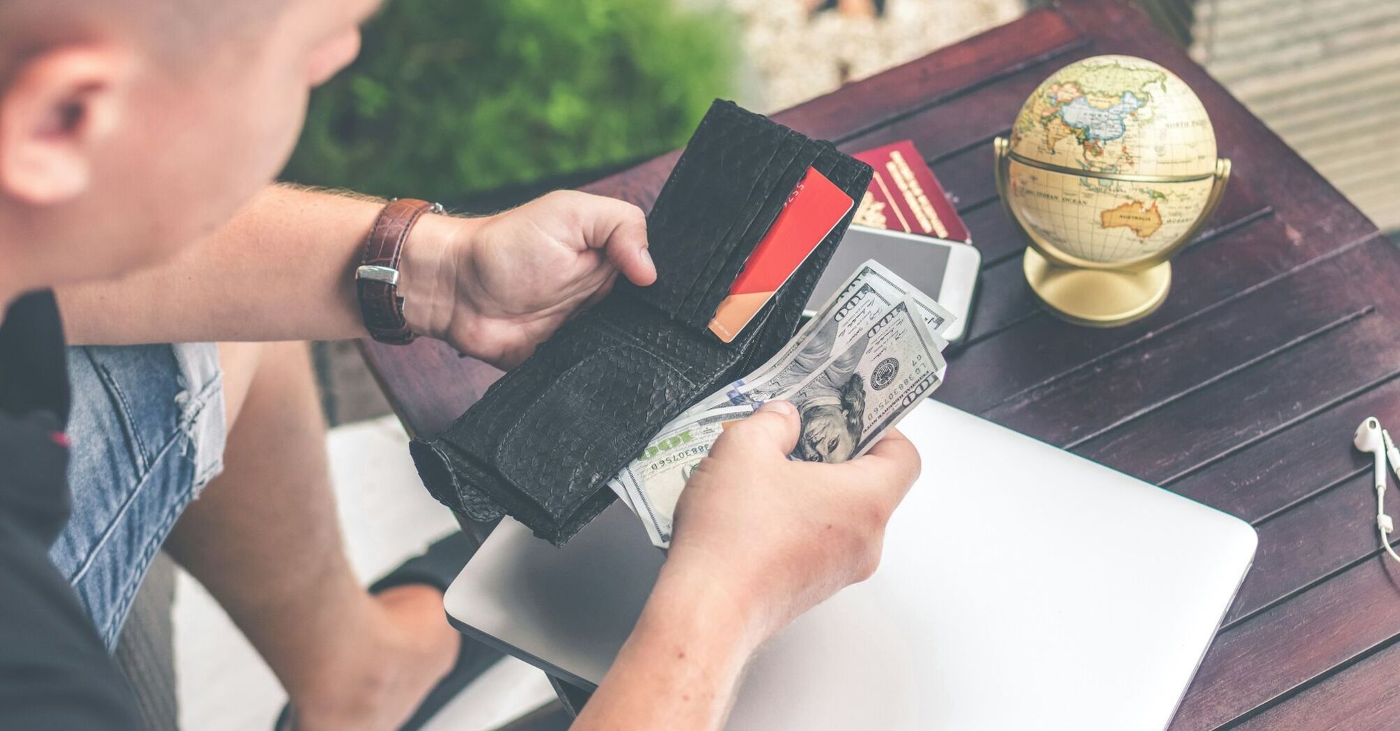 A traveler holding a wallet with cash and cards, preparing for a trip, with a globe and travel essentials on a table