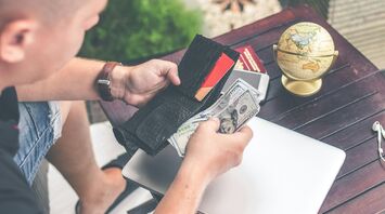 A traveler holding a wallet with cash and cards, preparing for a trip, with a globe and travel essentials on a table