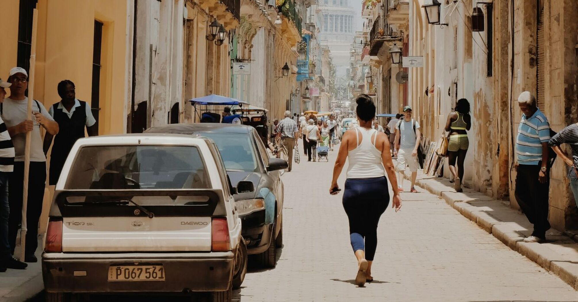 Narrow street in Havana with people walking under the sun