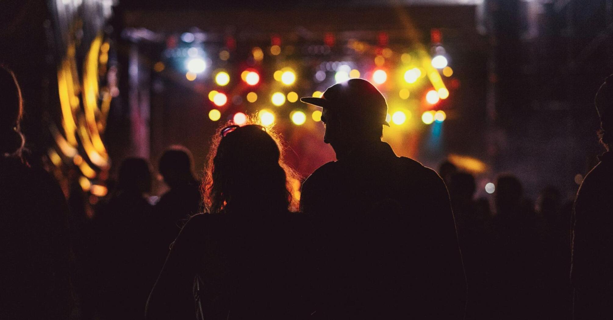 Silhouettes of people at a night event with colorful lights in the background