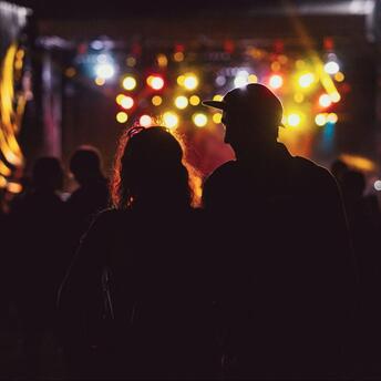 Silhouettes of people at a night event with colorful lights in the background