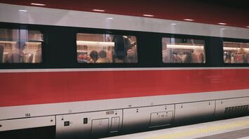 A red and white passenger train with people seated inside at a platform