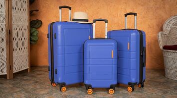 Three blue suitcases of different sizes, placed together, with a hat resting on top of the largest one