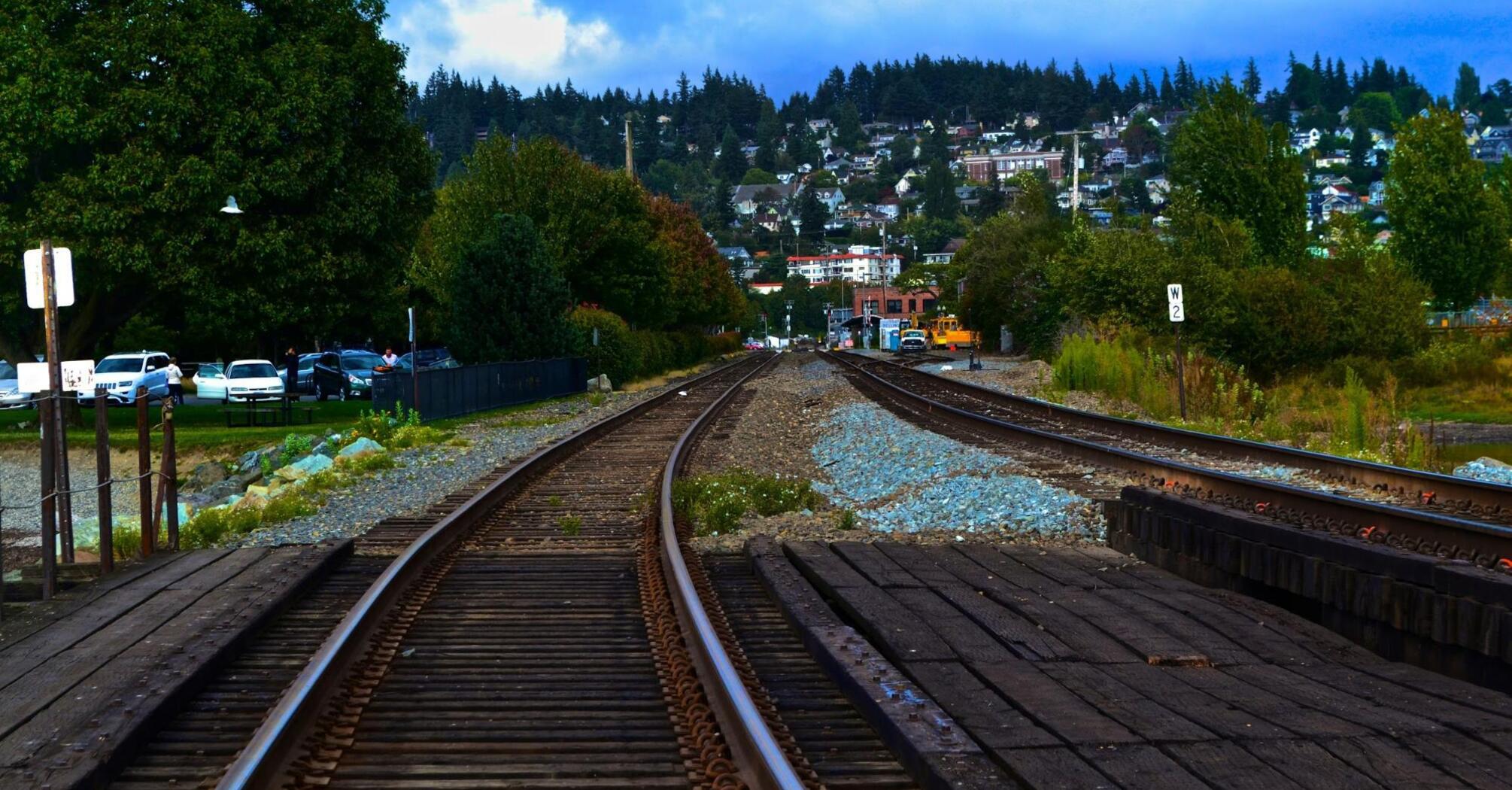 Railroad tracks extending towards a forested hillside town under cloudy skies