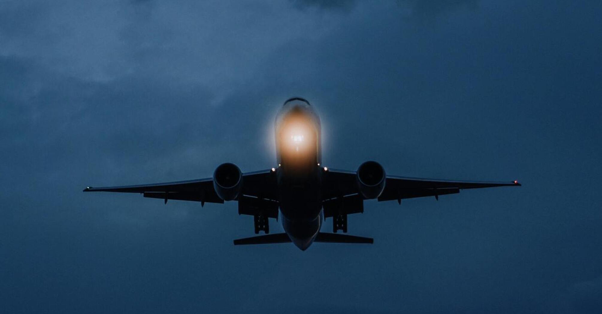 An airplane flying at dusk with illuminated lights, approaching landing