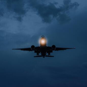 An airplane flying at dusk with illuminated lights, approaching landing