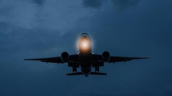 An airplane flying at dusk with illuminated lights, approaching landing