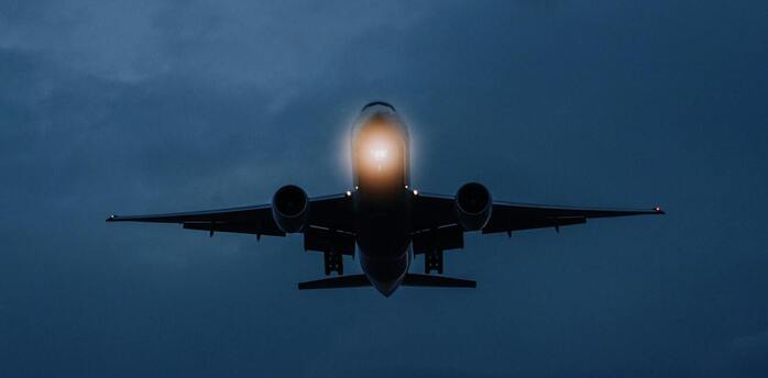 An airplane flying at dusk with illuminated lights, approaching landing