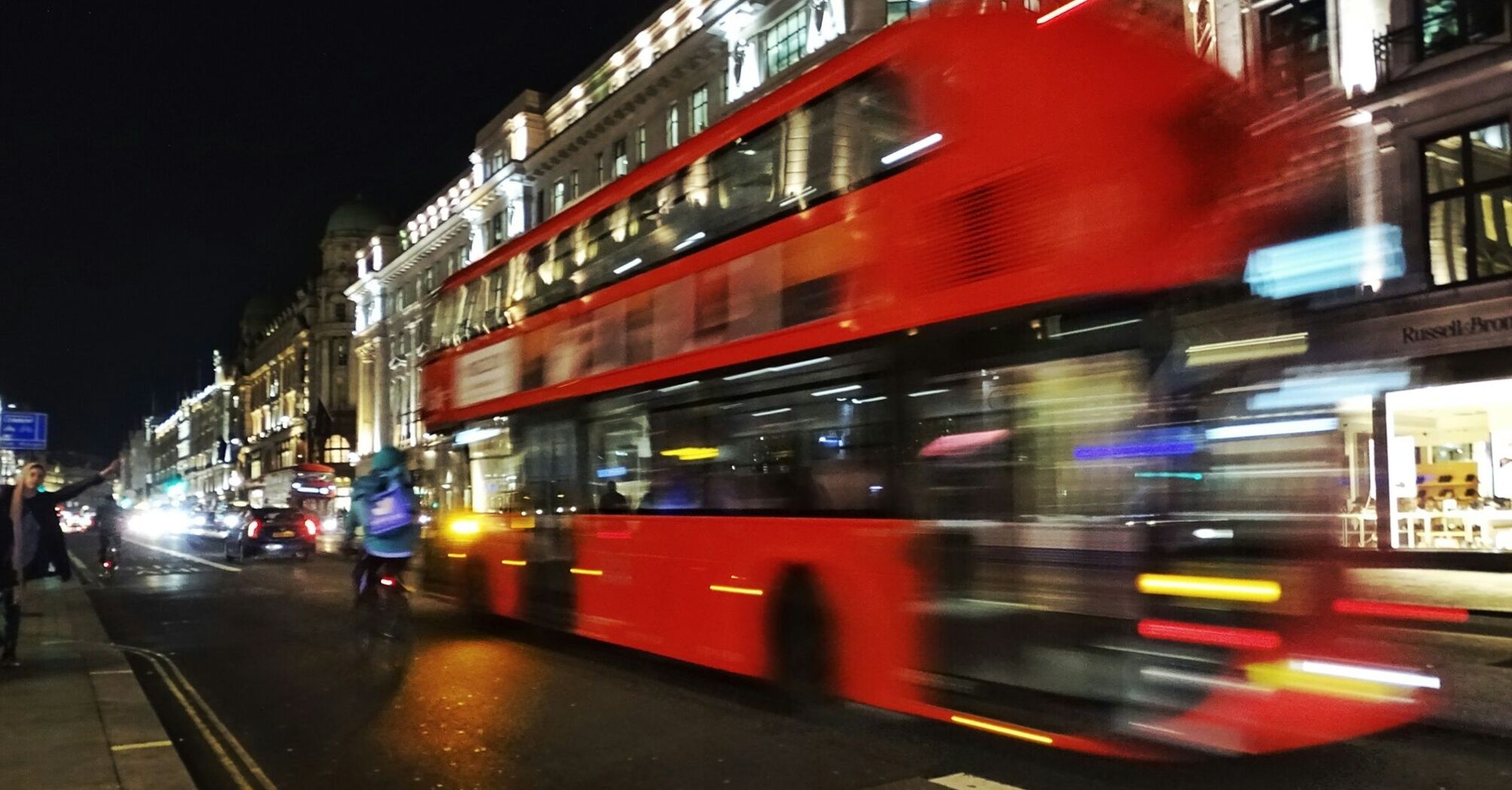 A red double-decker bus speeding through a busy city street at night